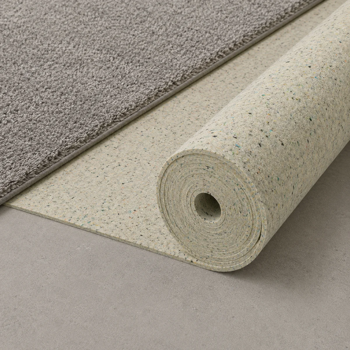 Aufgerollte Elitexa extra dichte Teppichunterlage unter einem grauen Teppich, die ihre robuste Materialstruktur und gleichmäßige Oberfläche zeigt.
