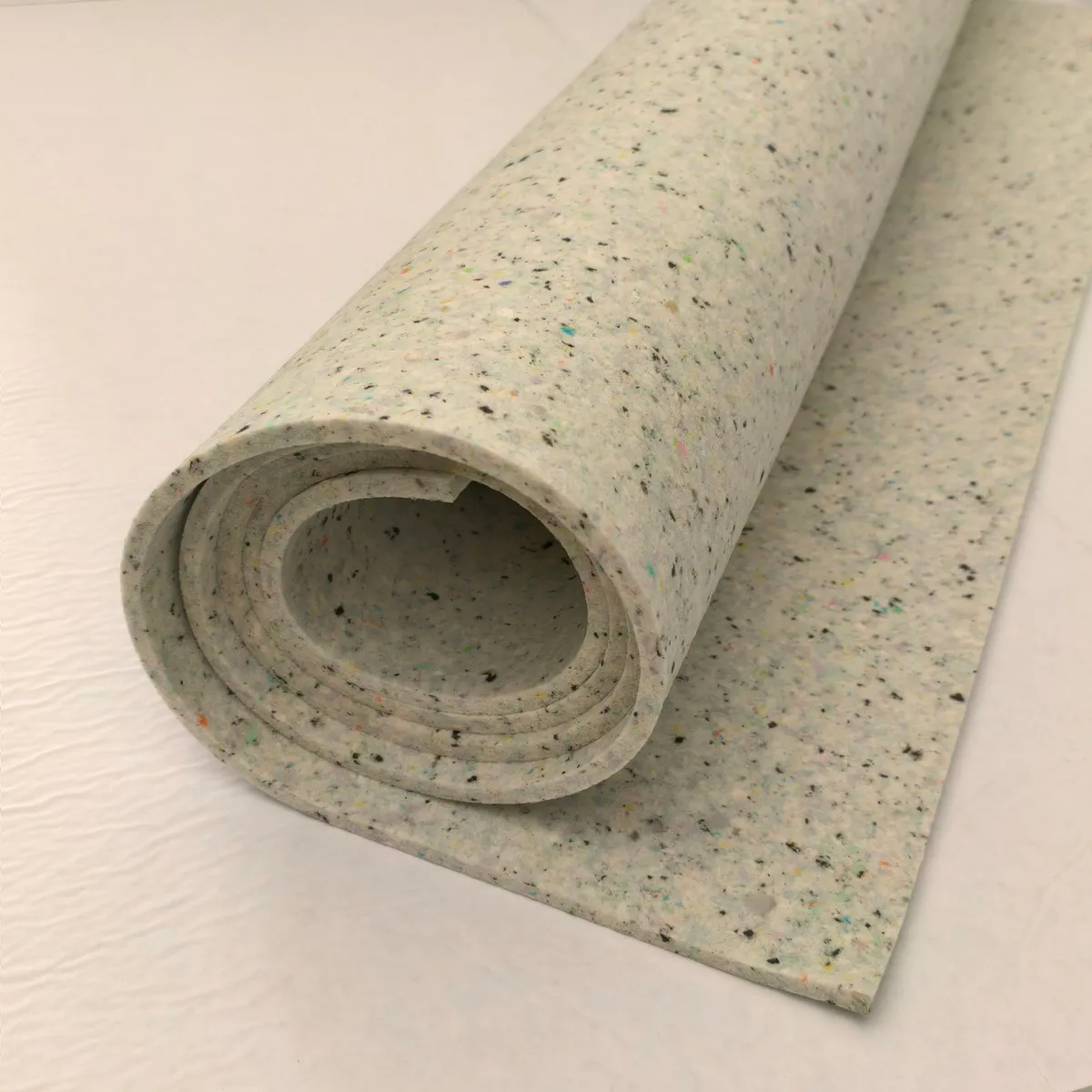 Aufgerollte Elitexa Teppichunterlage in Naturfarbe auf einer ausgerollten Bahn, mit gut sichtbarer Materialstärke und fein gesprenkelter, faseriger Oberfläche.
