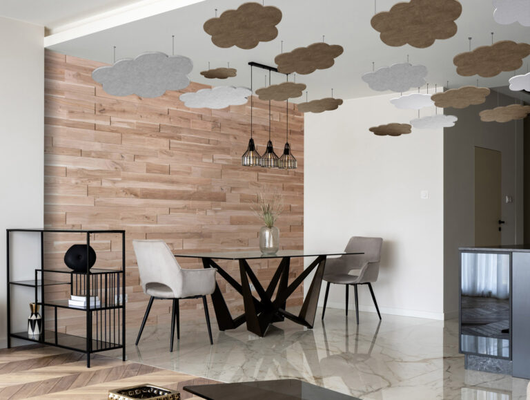Wolkenförmige Akustikpaneele in Braun und Weiß, abgehängt über einem Essbereich mit Holzwand und Marmorboden